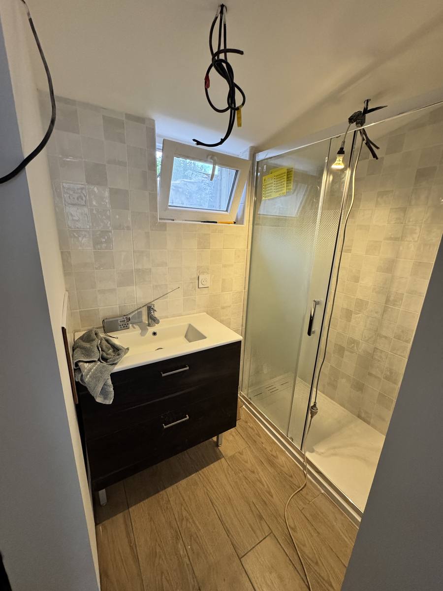 Salle d'eau de l'échoppe après rénovation : faïence claire, meuble-vasque et douche neufs, sol stratifié.