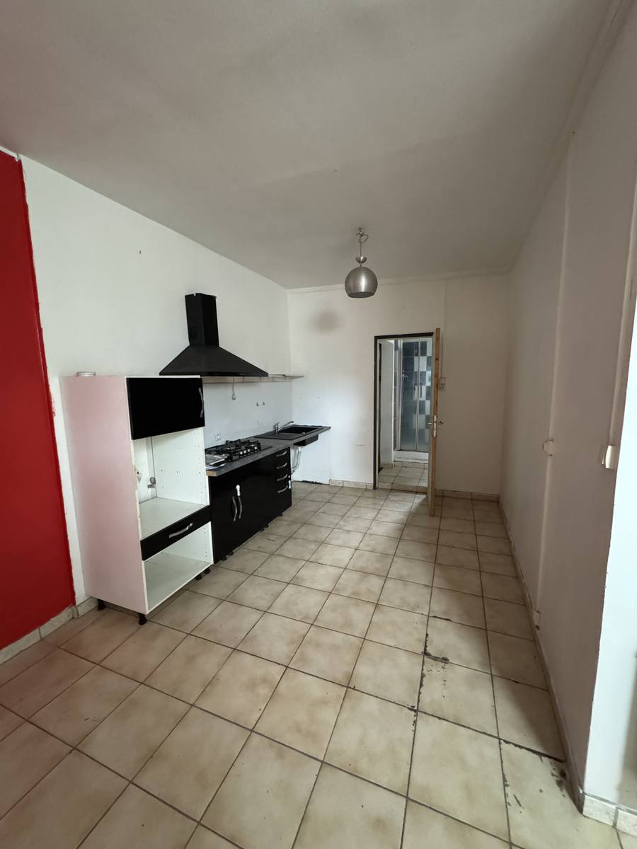 Séjour-cuisine d'une échoppe à Libourne avant travaux : mur rouge, ancienne gazinière et carrelage daté.